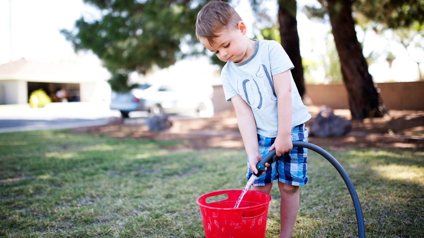 Boy filling up bucket with watering hose