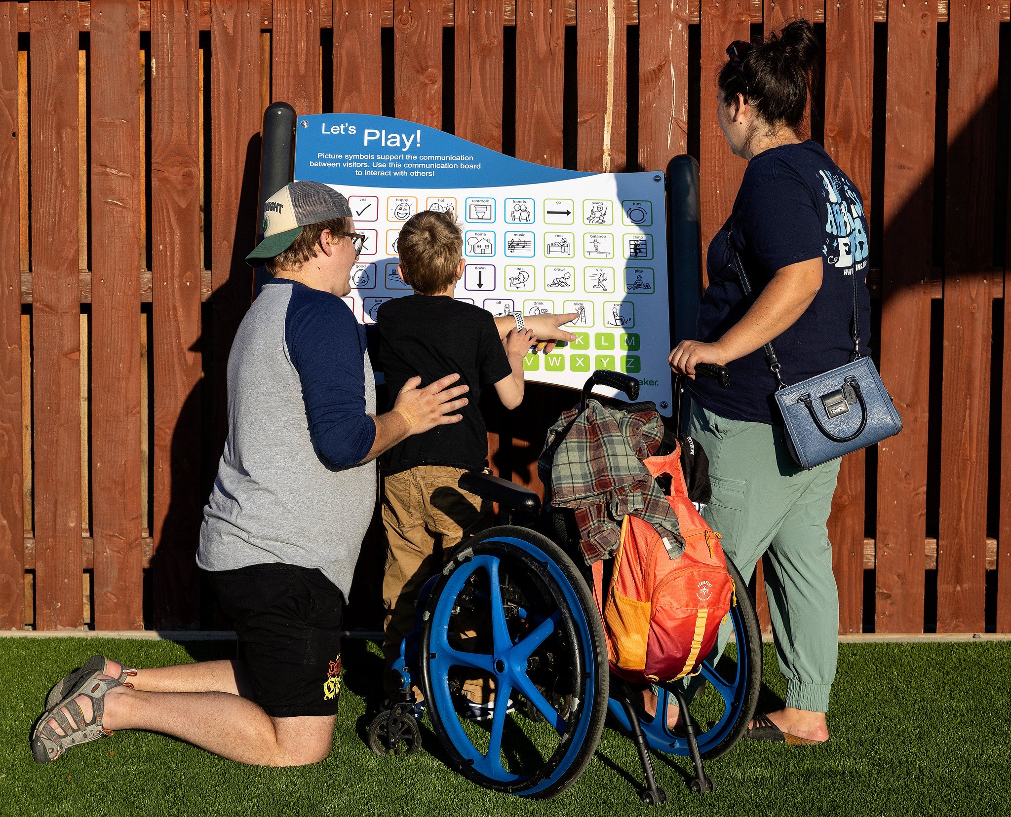 Mom and dad using an inclusive symbol board to interact with their son who is standing next to his wheelchair.