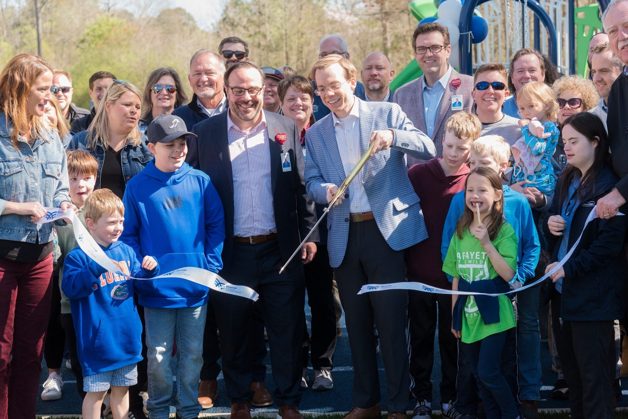 smiling faces as they cute a blue ribbon at a playground opening 