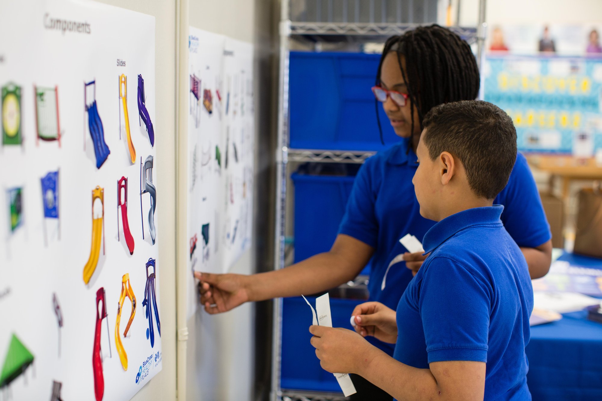 Boy and girl students looking at wall with lots of different playground options and putting stickers on the ones they like.