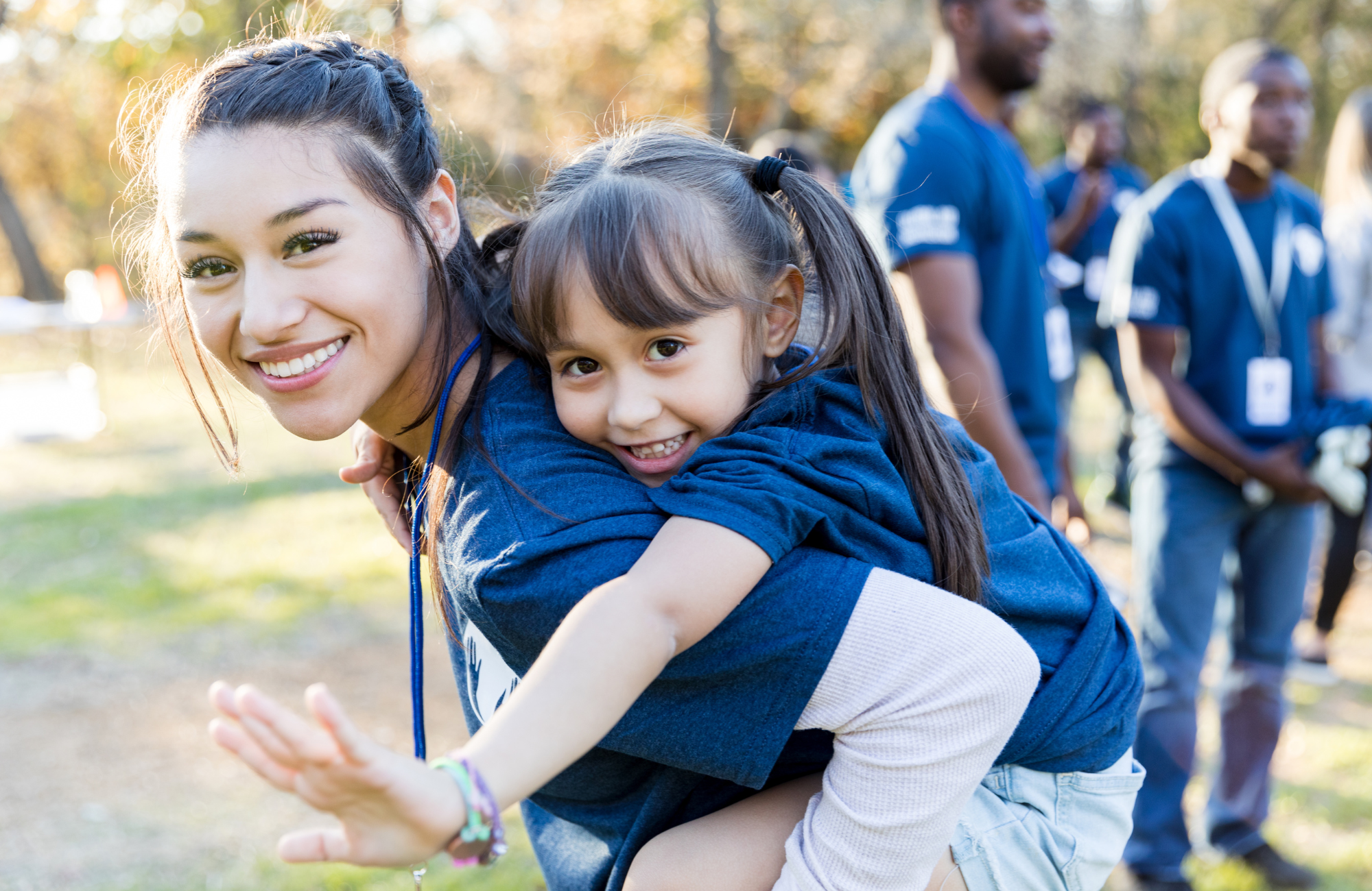 Woman with child on back, in volunteer shirts in park