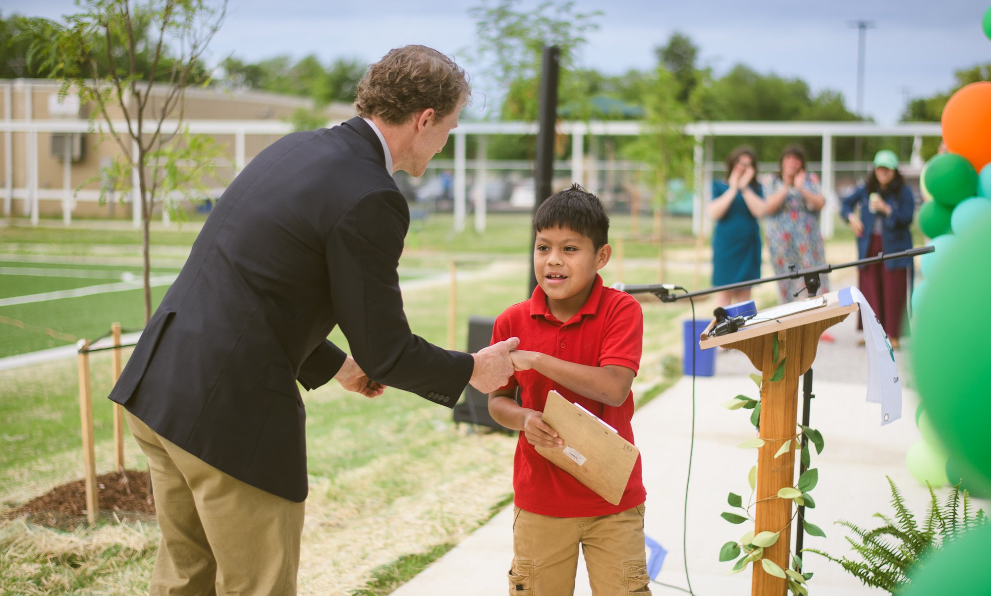 Man shaking hand of young boy who was the speaker at a TPL park grand opening. 
