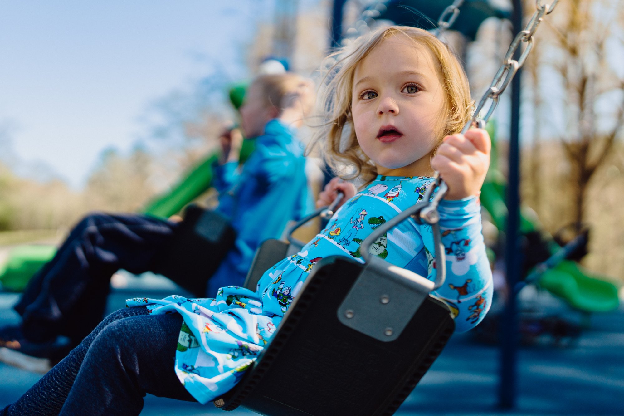 Young child wearing a blue toy story shirt swinging 