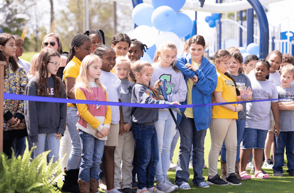 Children gathered together to cut a blue ribbon.