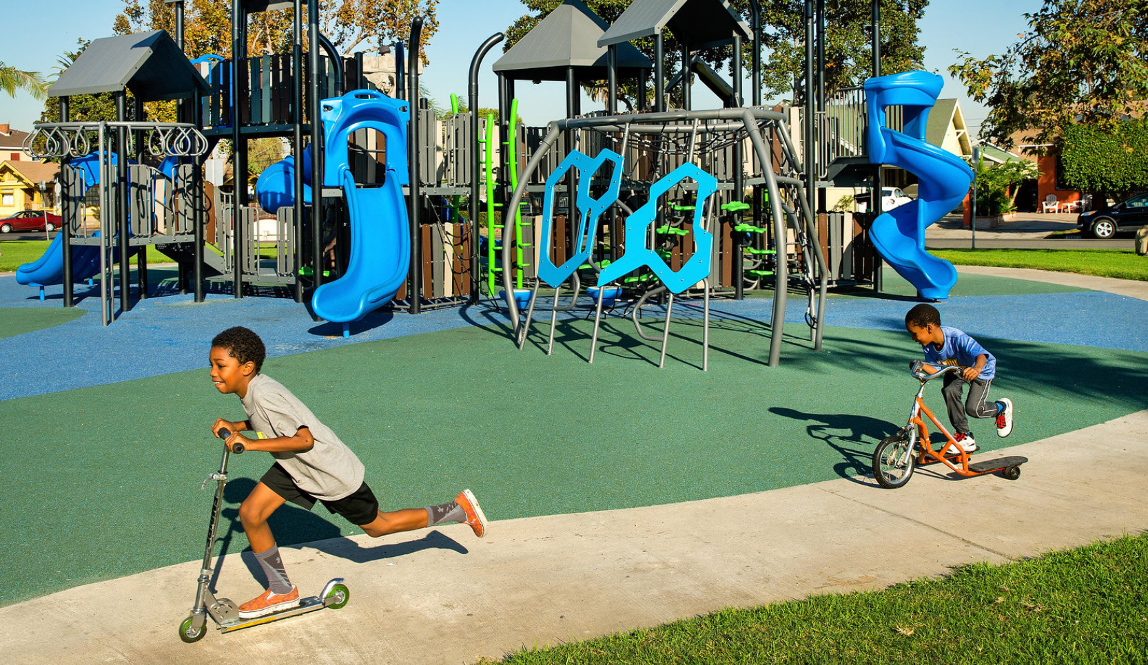 Kids riding scooters on path around playground at park