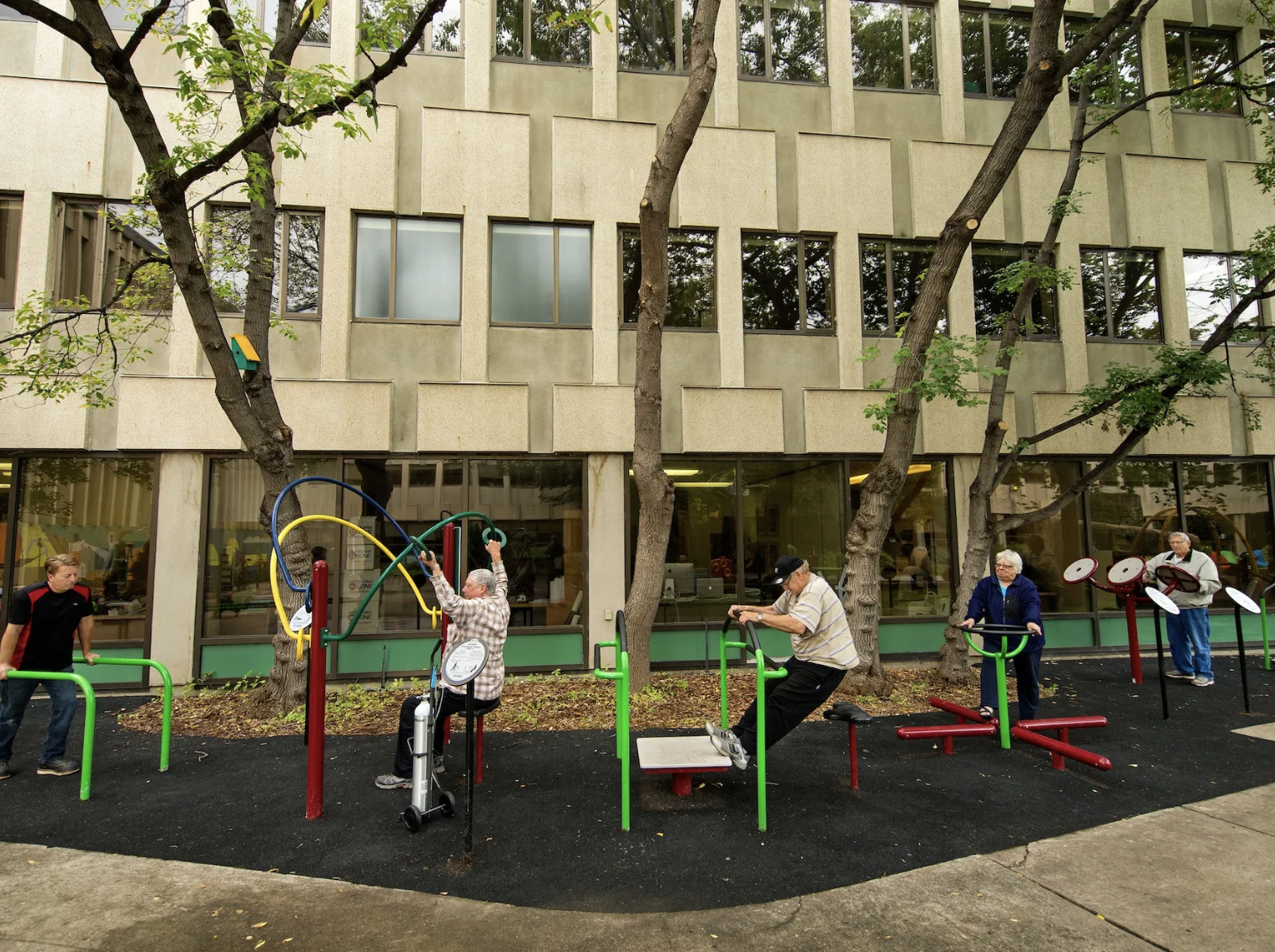 Group of elders using fitness equipment outside of building Group of elders using fitness equipment outside of building
